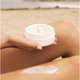Person applying kai body butter cream to their leg on a beach.