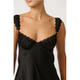 A close-up of a model wearing a black satin slip dress with ruffled shoulder straps and a lace-trimmed sweetheart neckline.