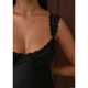 Close-up of a person wearing a black satin slip dress with lace trim and ruffled shoulder details, shown against a dark brown wooden background.