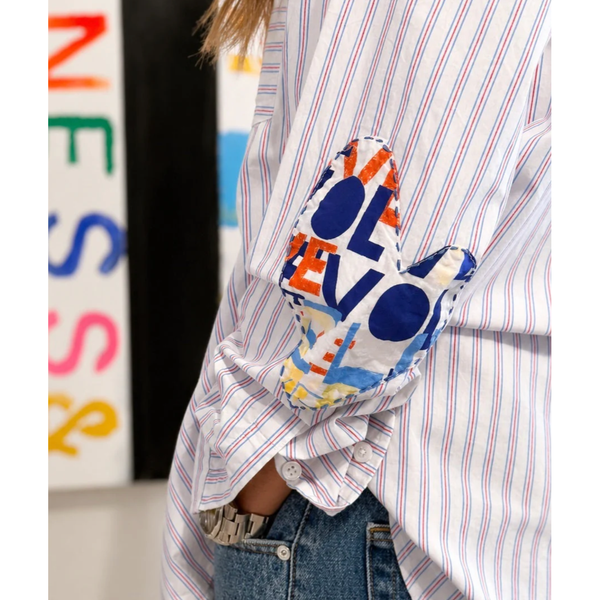 Person wearing a colorful 'LOVE' shirt over a striped shirt with a blurred background.