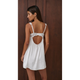 A woman shown from the back wearing a white satin slip dress with lace trim and an open back, standing against a dark brown wooden wall.