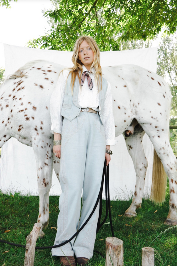 women standing in front of a horse wearing a bandana around her neck with light wash denim vest, white blouse and light wash denim jeans