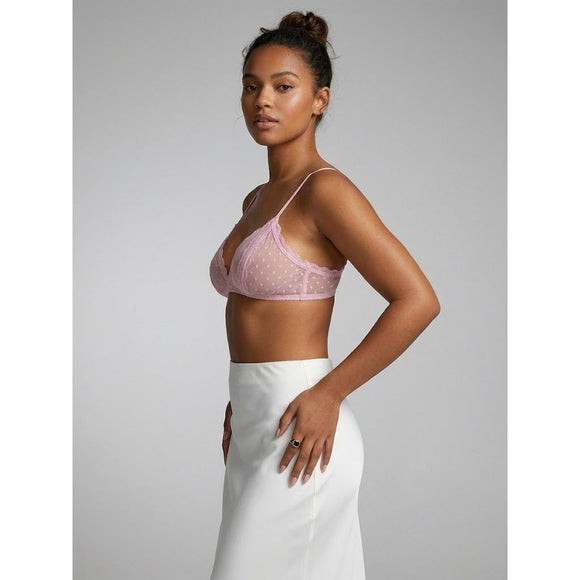 A woman modeling a light pink sheer mesh bralette with white polka dots, paired with a white skirt, against a solid gray studio background.